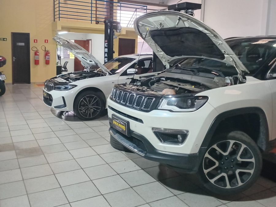 BMW Série 3 e Jeep Compass brancos com o capô aberto no salão da oficina