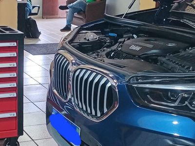 BMW azul com o capô aberto e a recepção da oficina ao fundo
