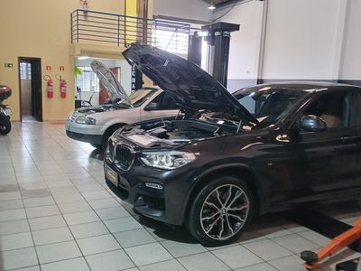 BMW X4 preto com o capô aberto entre os elevadores da oficina